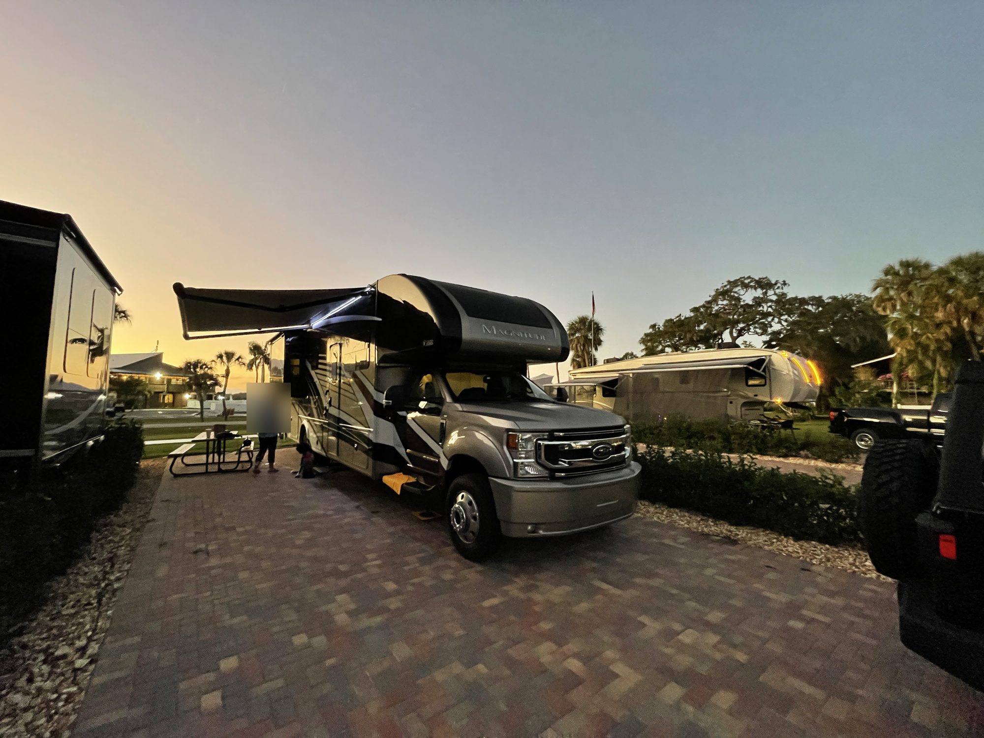 The motorhome at sunset with the awning out and its lights on